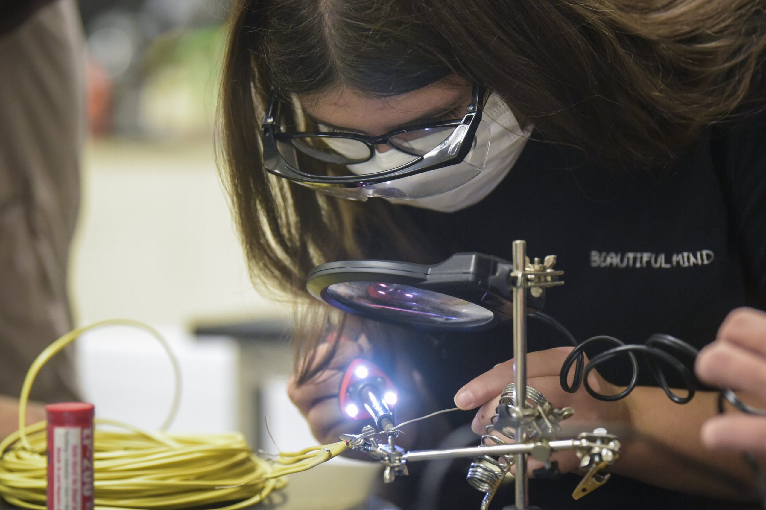 Student looking through magnifying glass while soldering