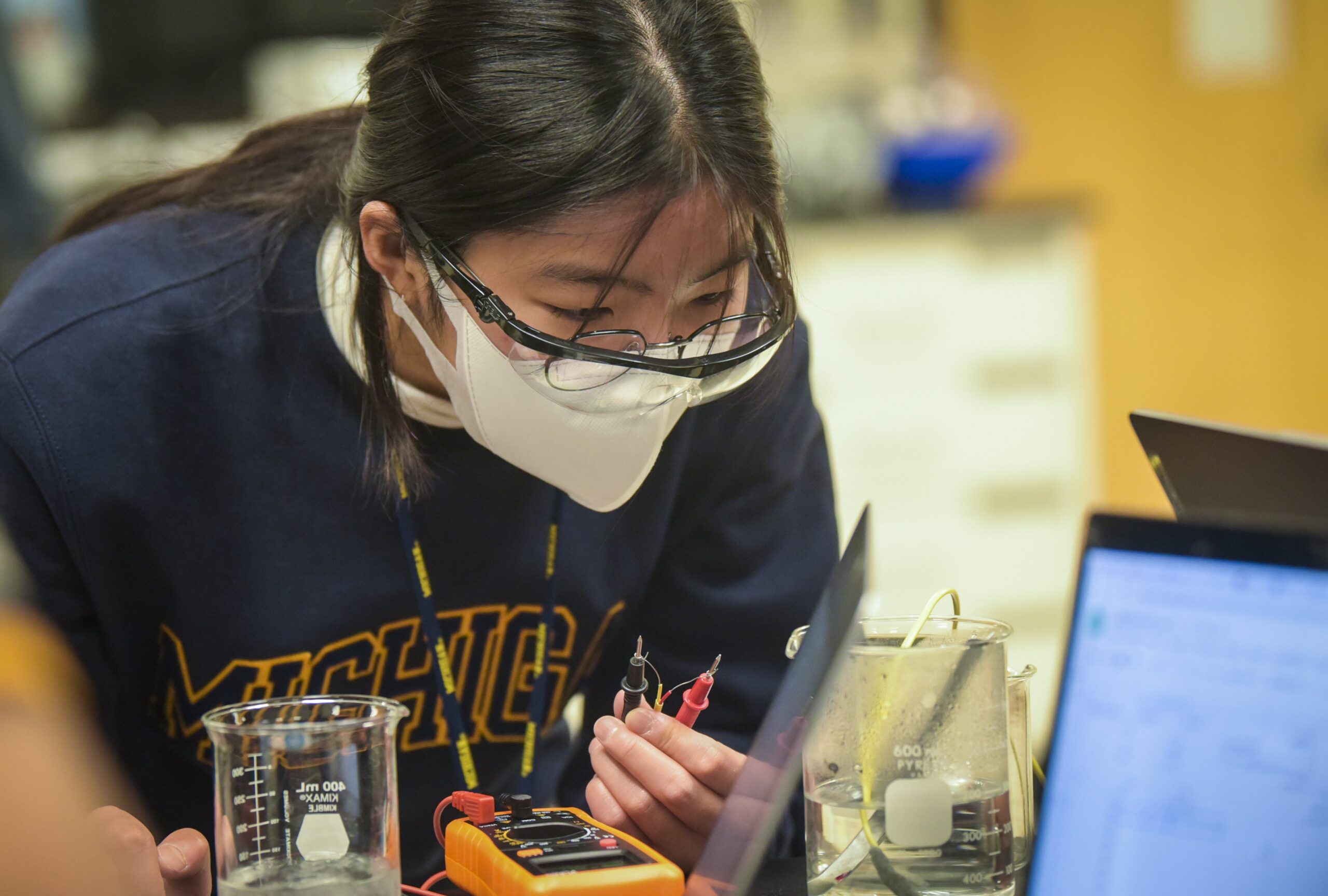 Student using multimeter while viewing laptop screen