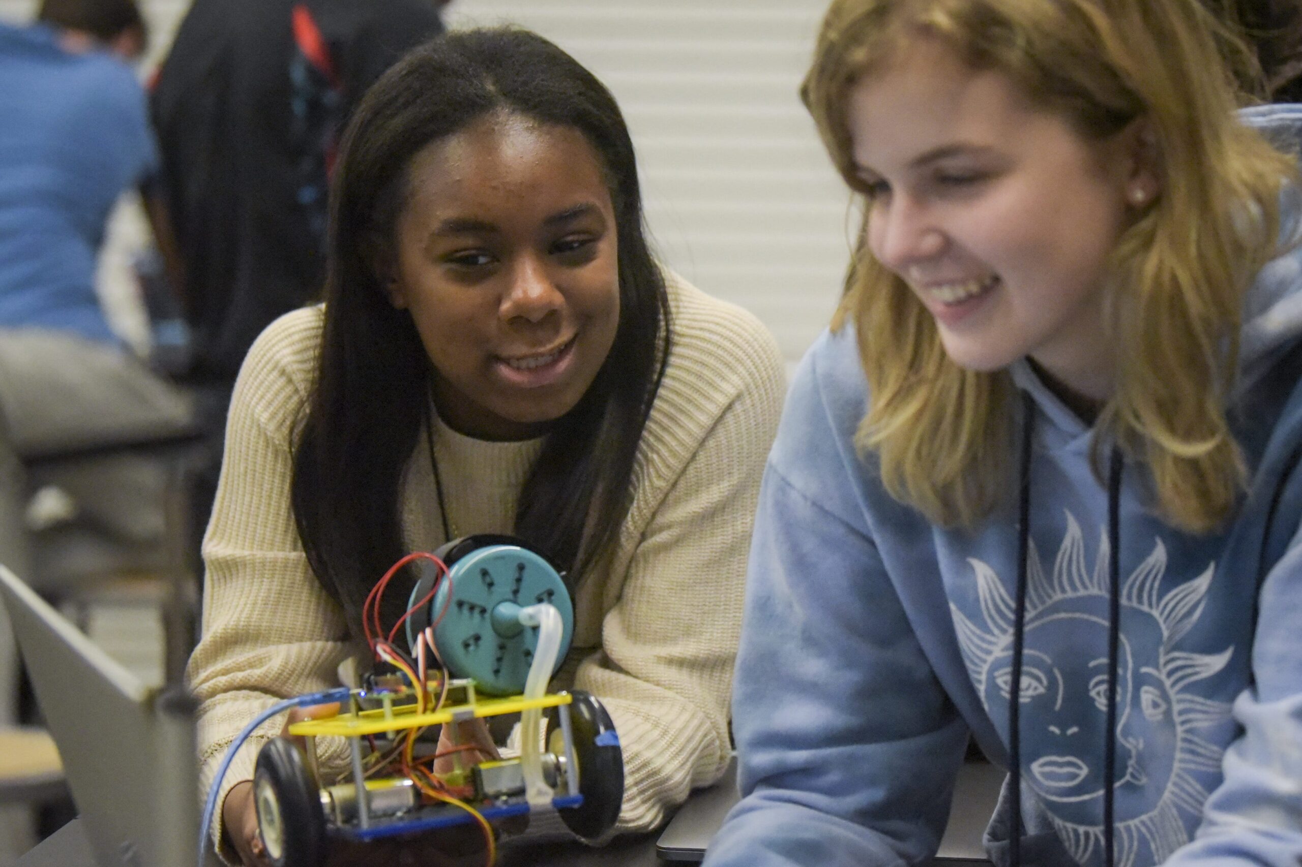 Student holding robot while other works on laptop
