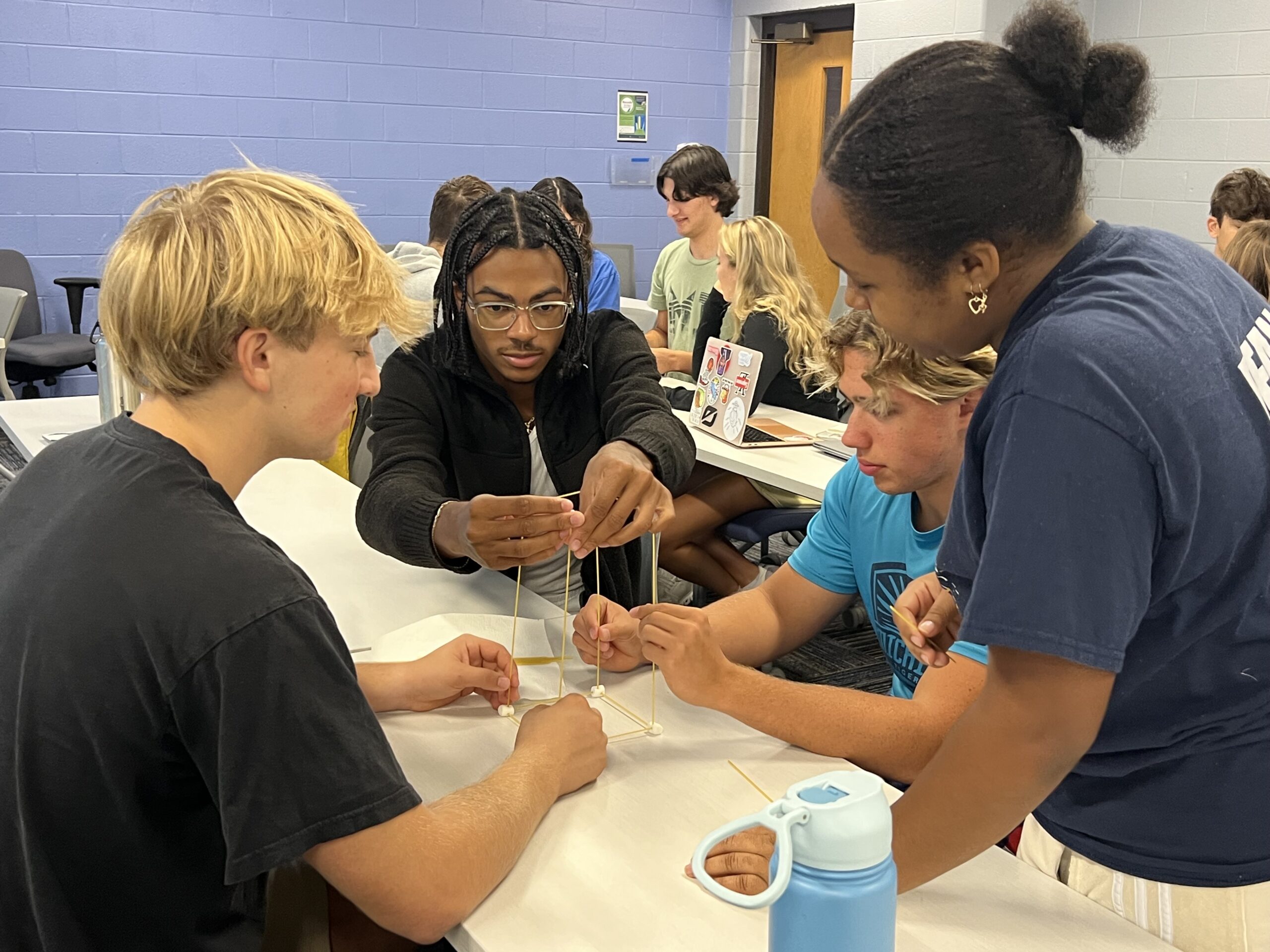 Three students wearing goggles looking at one laptop screen