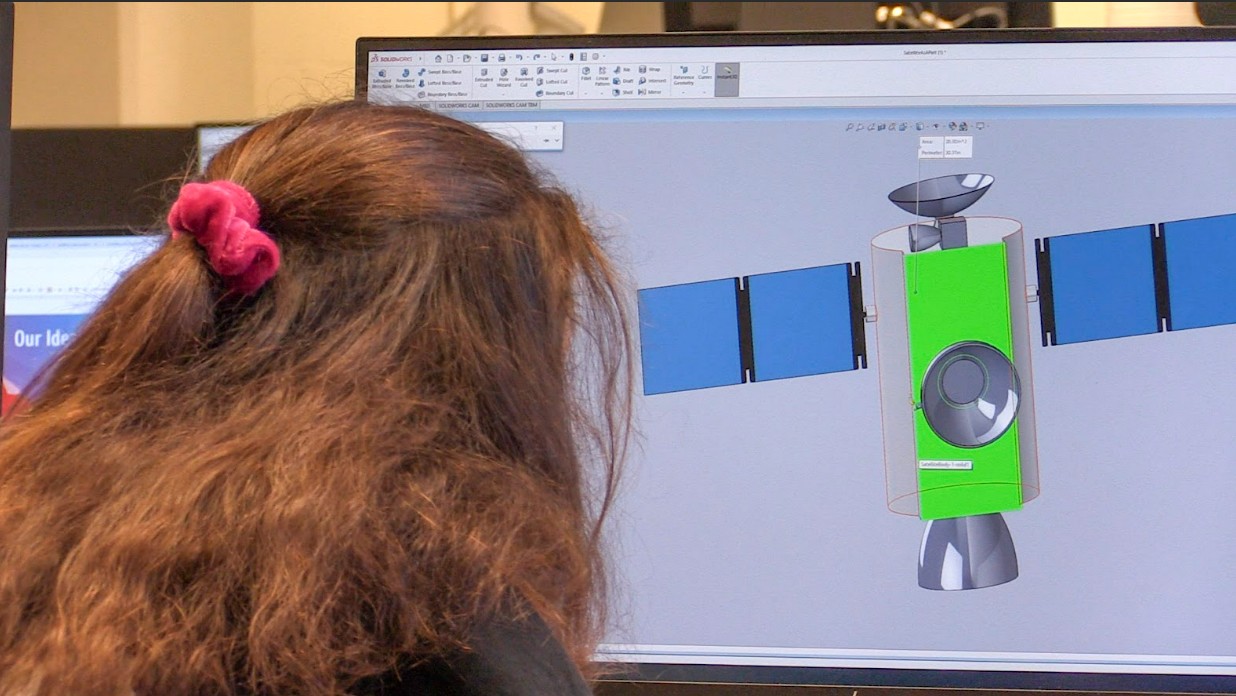 Three students in goggles smiling and looking at laptop screen